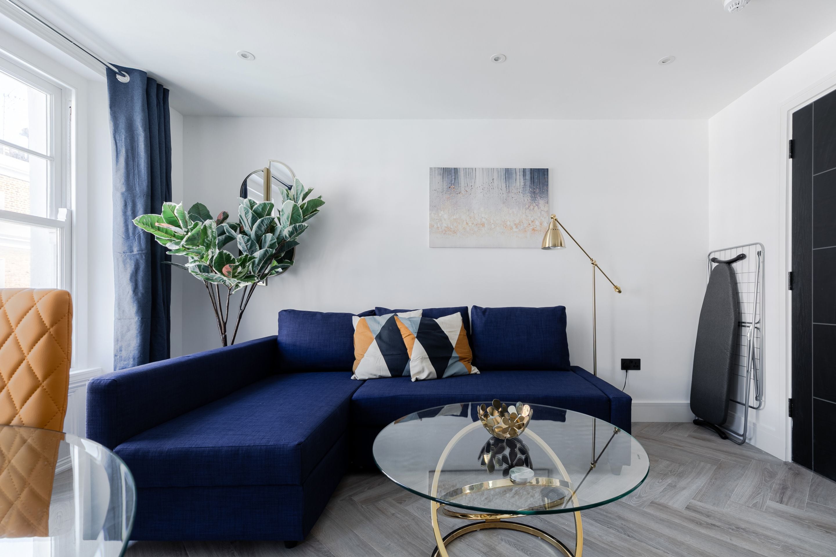 Una sala de estar moderna con un sofá seccional azul, una mesa de centro de vidrio y una planta grande.