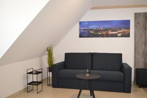 Een moderne woonkamer met een donkergrijze bank, een klein rond tafeltje en een stadslandschap op de muur.