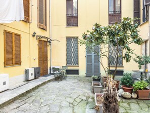 A courtyard with a stone floor, wooden shutters, a table with chairs, and potted plants. - LikeYourHome (Vercelli)