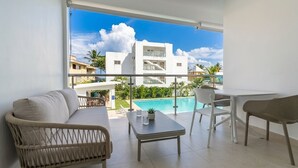 A balcony with a pool view, a sofa, a table, and chairs. - Cabarete Apt: Pool, Steps to Beach (Cabarete)