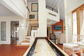 A spacious living area with a shuffleboard table, a staircase, and a television mounted on the wall.