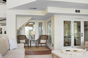 Un salon comprenant un canapé, deux fauteuils en osier, une petite table avec une lampe et une porte-fenêtre coulissante donnant sur un balcon.