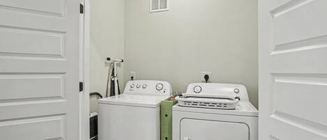 A laundry room with two washing machines and a dryer, a ventilation vent on the wall, and a door leading to another room.
