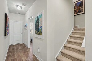 A hallway with a wooden floor, a white door, and a staircase with beige carpet. - Osprey Cove | Townhouse in Ocean Isle Beach (OCEAN ISL BCH)