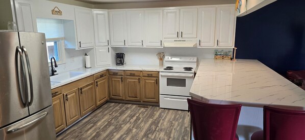 A kitchen with white cabinets, a stainless steel refrigerator, a white stove, and a marble countertop.
