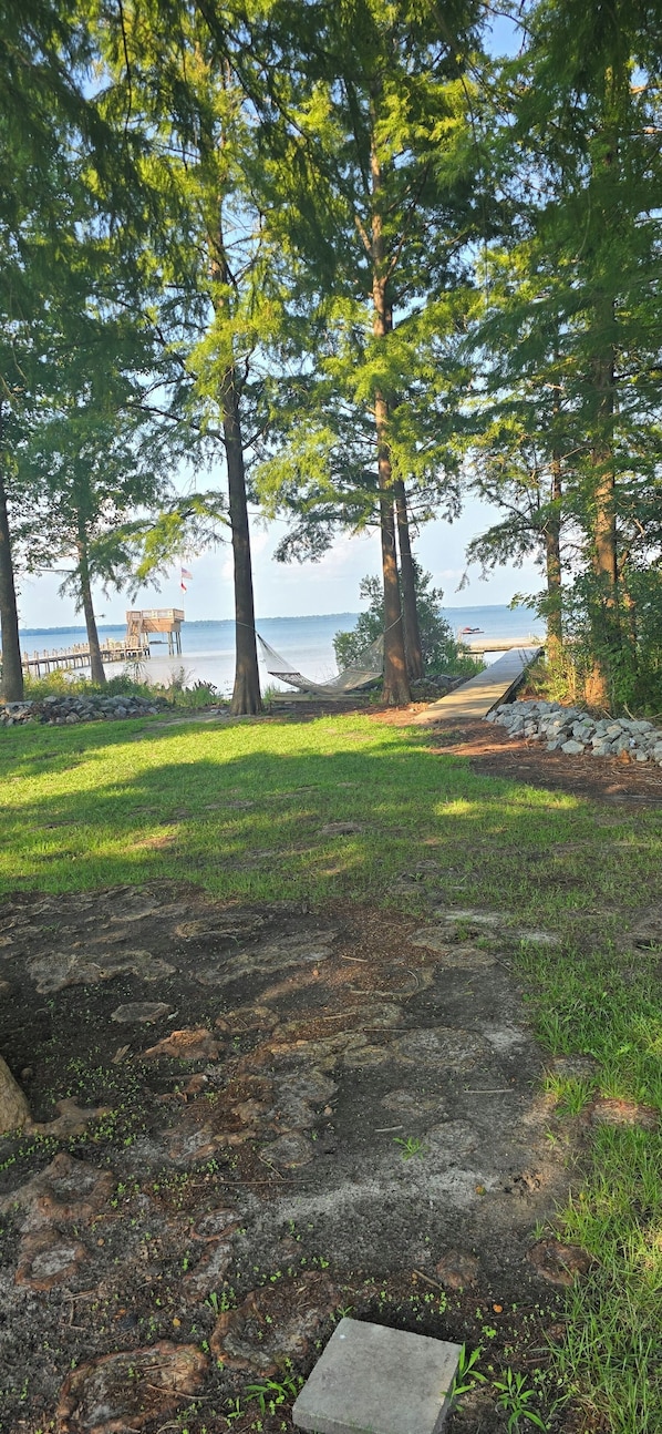 A grassy area with a hammock, a wooden structure, and a view of the water.