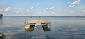 A wooden pier extending into calm water with a flag on a pole to the left.