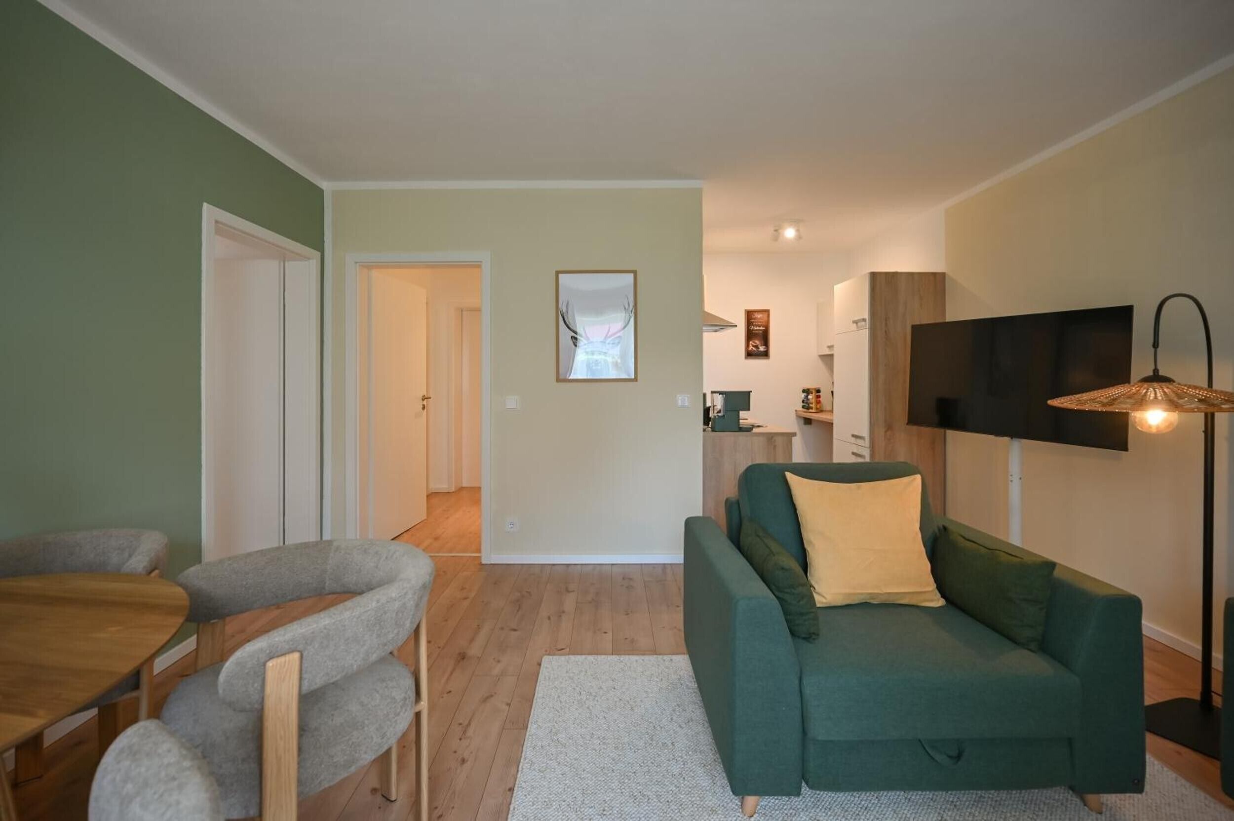 A living room with a green sofa, a dining area with a wooden table and chairs, and a kitchen in the background.