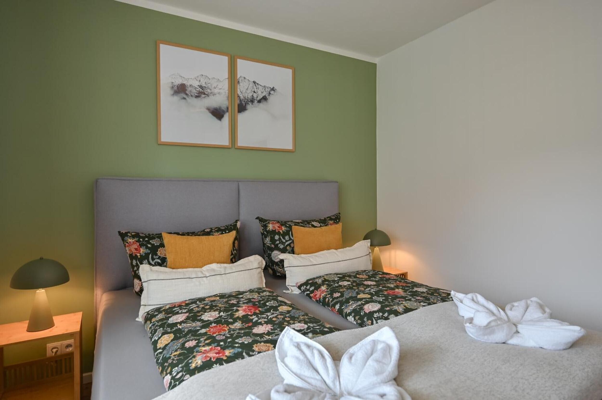 Ein Doppelbett mit Blumenmuster, zwei Kissen, ein Nachttisch mit Lampe und ein Wandbild.