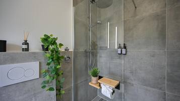Ein modernes Badezimmer mit einer gläsernen Dusche, einem wandmontierten WC und einer kleinen Ablage mit einer Pflanze.