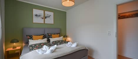 Un dormitorio con una cama, dos lámparas de noche, una obra de arte en la pared y una puerta.
