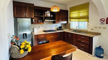 A kitchen with a wooden table, two chairs, a refrigerator, cabinets, and a hanging light fixture.