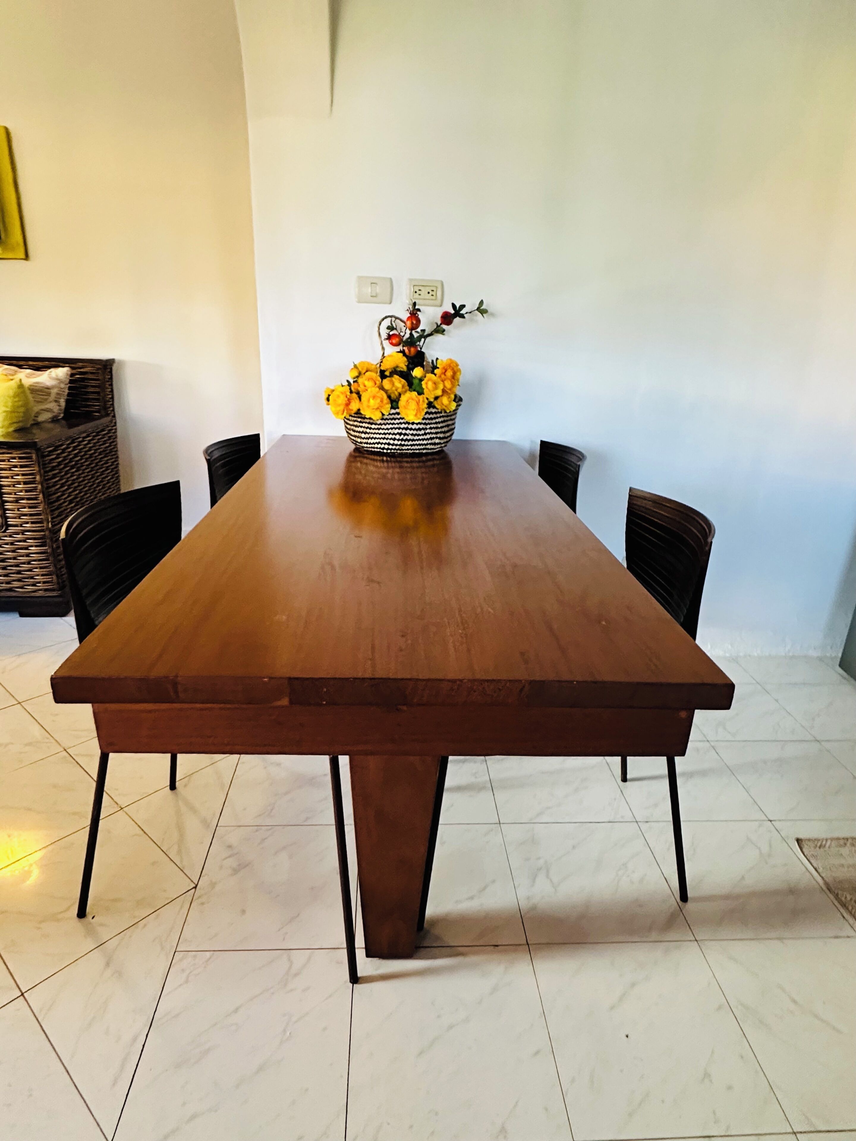 A dining table with chairs, a vase of yellow flowers, and a wall socket.