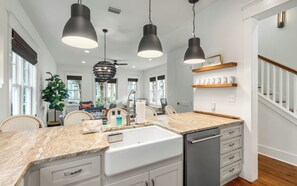 Une cuisine dotée d’un plan de travail en marbre, de meubles blancs, d’un lave-vaisselle et de luminaires suspendus.
