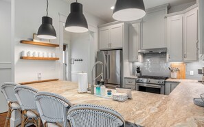 A modern kitchen with a marble island, stainless steel appliances, and wicker chairs. - Tangerine Dream: Pools, Beach & Tennis (Panama City Beach)