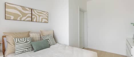 A bedroom with a bed, pillows, a bedside table, and a wall-mounted artwork.