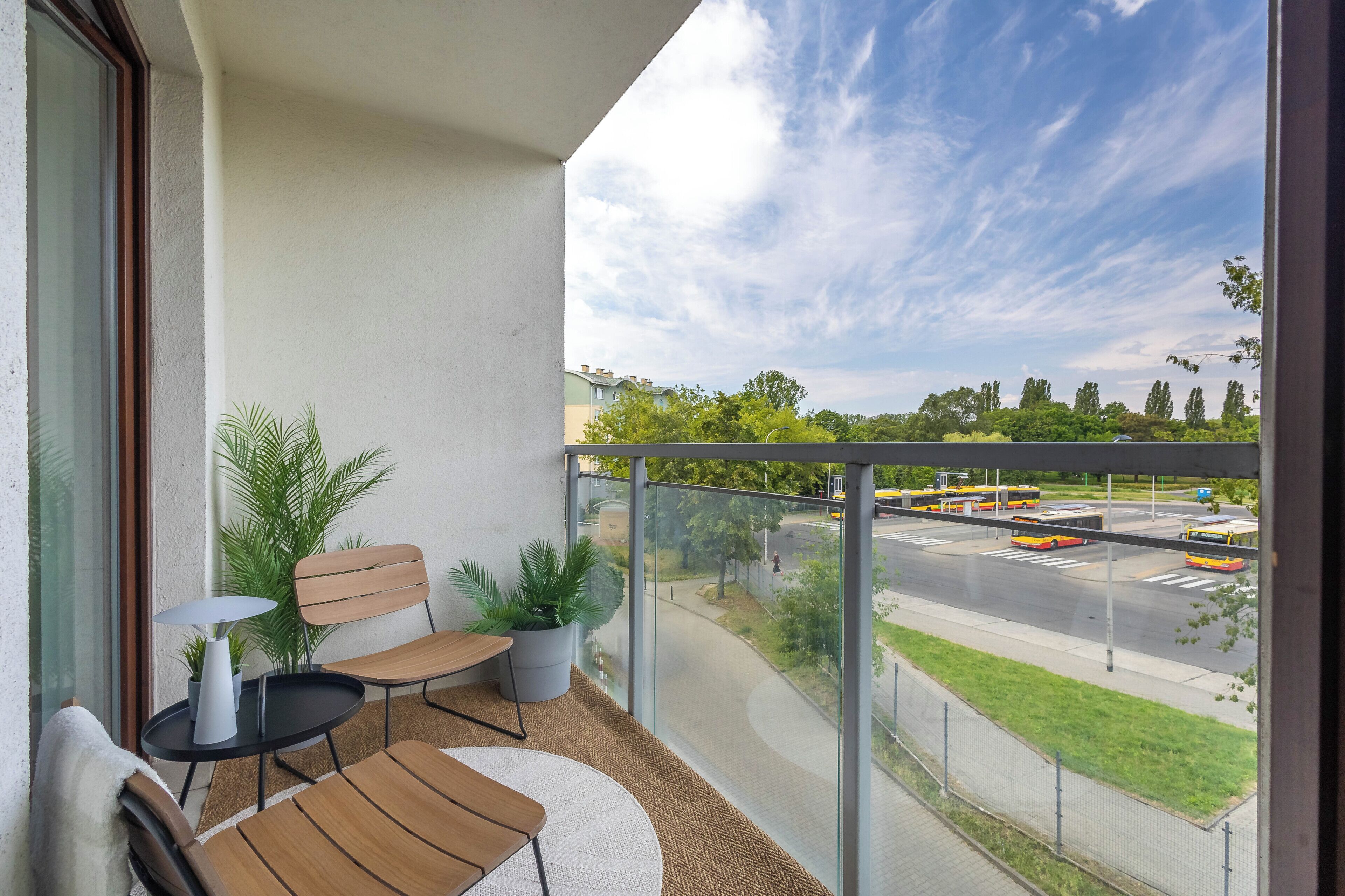 Un balcon avec un espace salon, une vue sur une route où circulent des autobus, et de la verdure en arrière-plan.