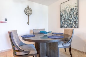 A dining area with a round table, four chairs, a wall clock, and a framed artwork. - Vicky's Beach Front Oasis (Luquillo)