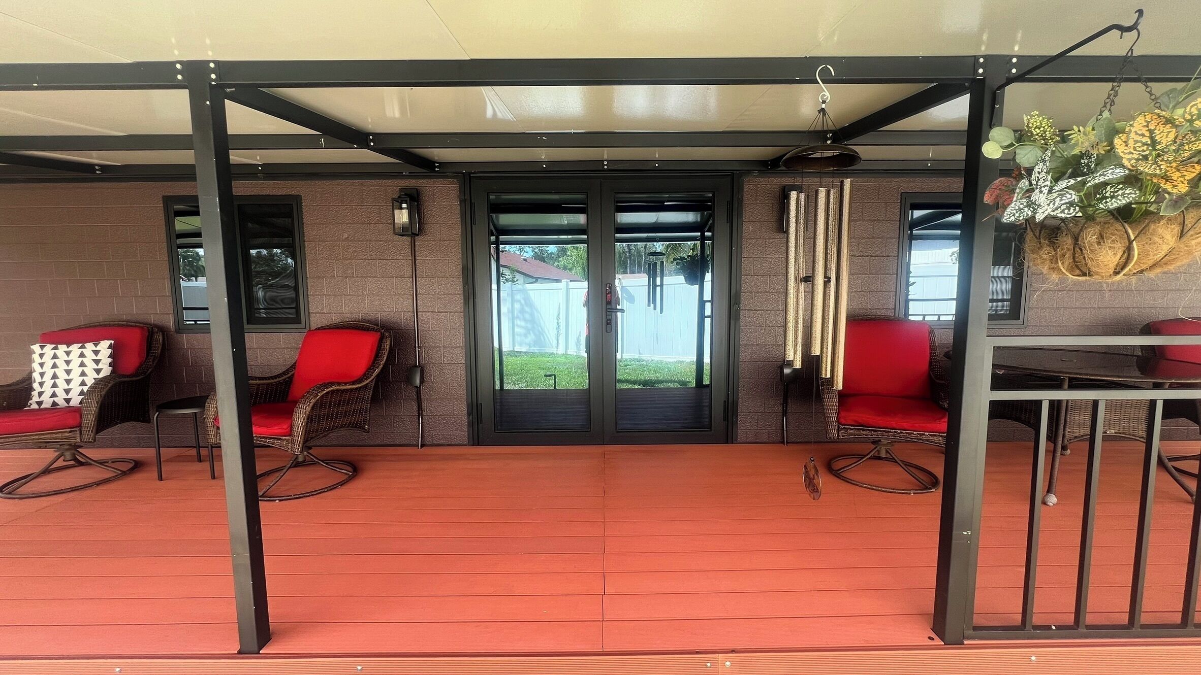 Un patio couvert avec des fauteuils en osier et une table, une porte-fenêtre coulissante et une plante suspendue.