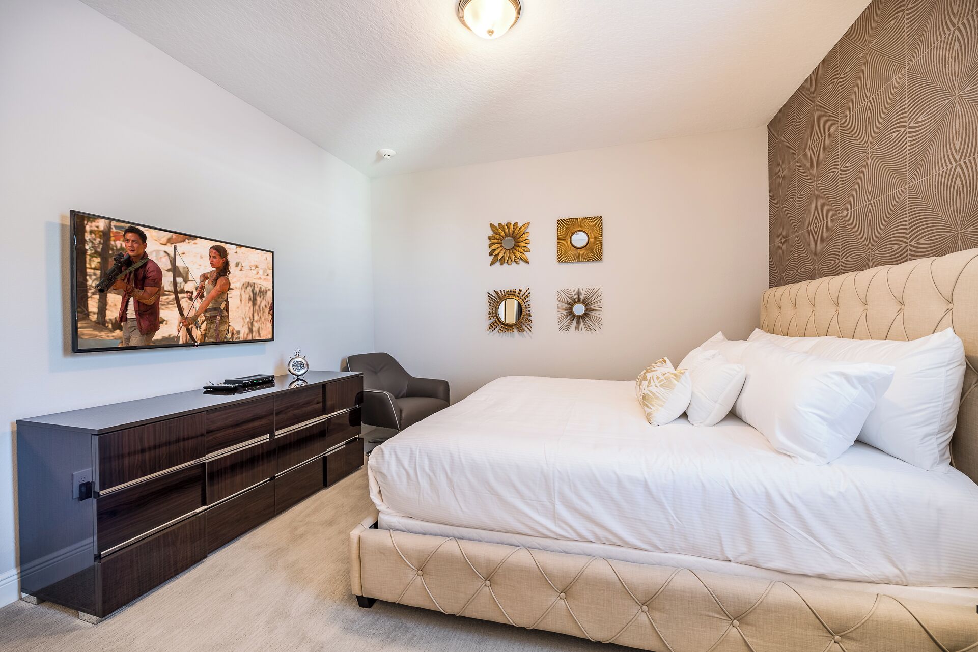 Une chambre à coucher comprenant un lit, un téléviseur, une commode et des miroirs décoratifs sur les murs.