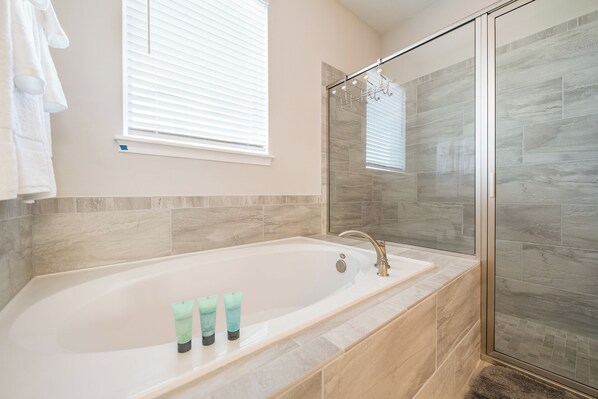Ein Badezimmer mit Badewanne, einer Duschkabine aus Glas und einem Fenster mit Jalousien.
