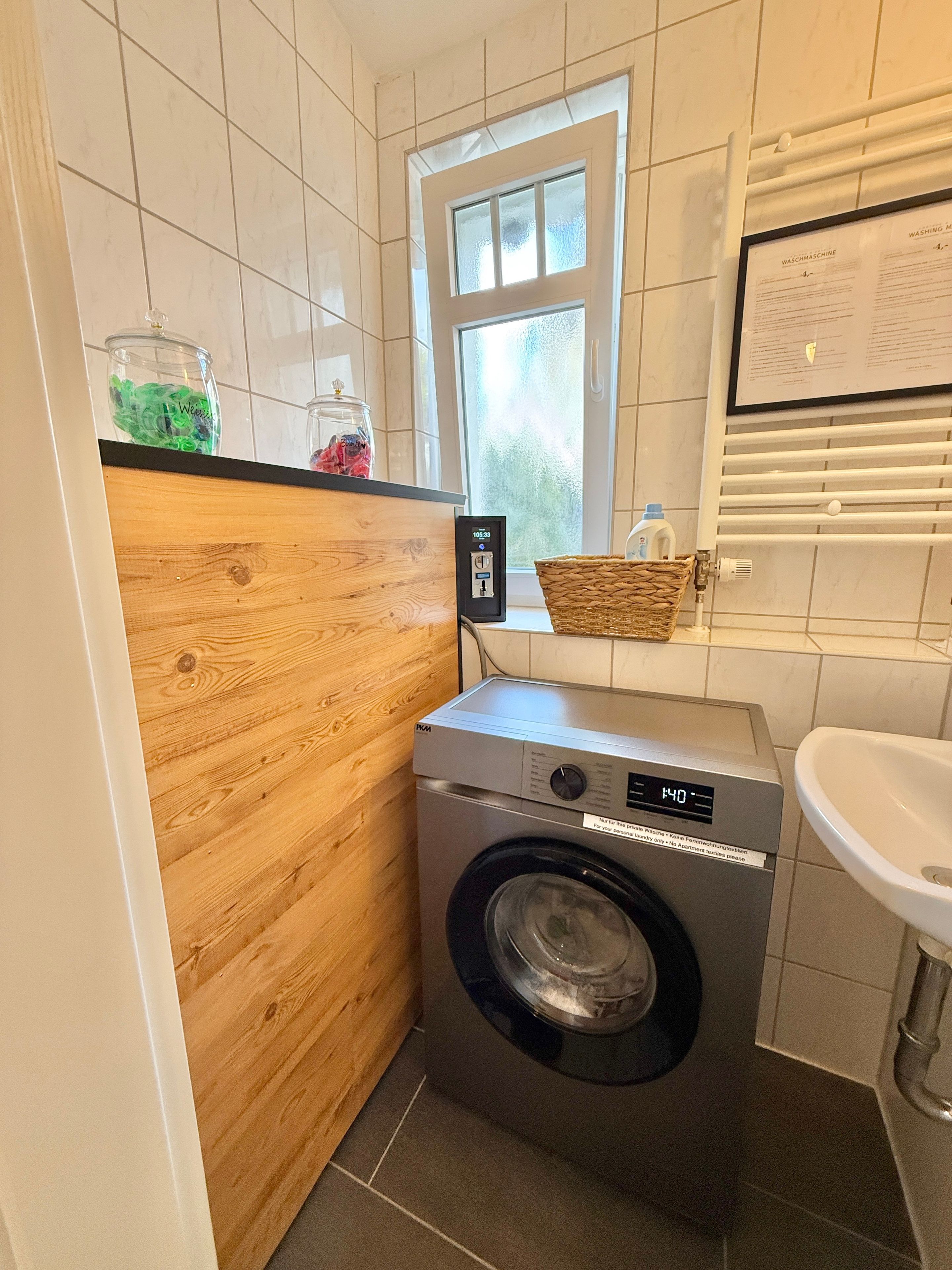 A compact laundry area with a washing machine, a wooden cabinet, a window, and a sink.