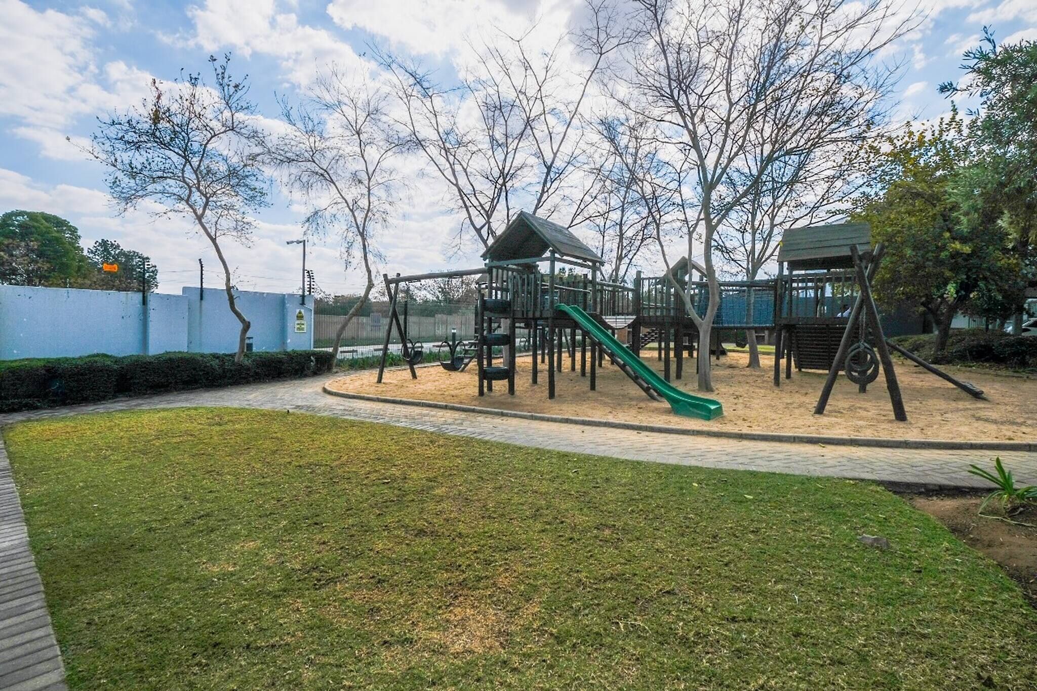 A playground with a slide and climbing structures, surrounded by a grassy area and trees.