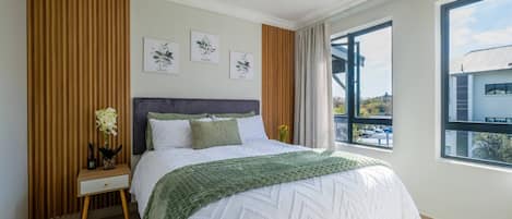 A bedroom with a bed, a nightstand, a window, and wall art.