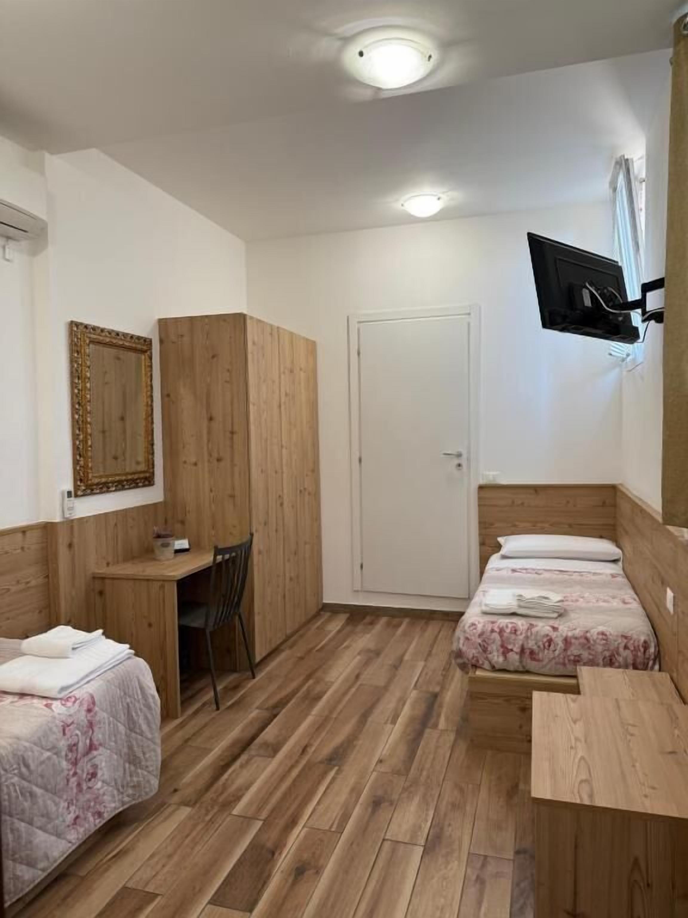 Una habitación con dos camas, un escritorio, una silla, un televisor montado en la pared y una puerta.