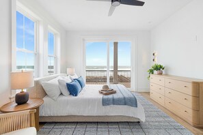 A bedroom with a bed, a nightstand, a dresser, a window with a view of the beach, and a ceiling fan. - Sea Spray East | Oceanfront Duplex with Private Pool + Elevator (Emerald Isle)