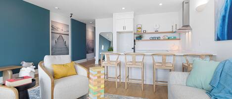 A modern living room with a sofa, a coffee table with a jigsaw puzzle, a kitchen area with bar stools, and a dining table.