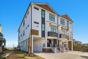 A multi-story residential building with a balcony on the second floor, a covered entryway, and a staircase leading to the main entrance. - Sea Spray East | Oceanfront Duplex with Private Pool + Elevator (Emerald Isle)