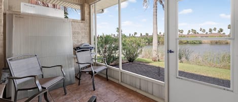 A covered patio with a view of a lake, outdoor seating, and a door leading to the outside.