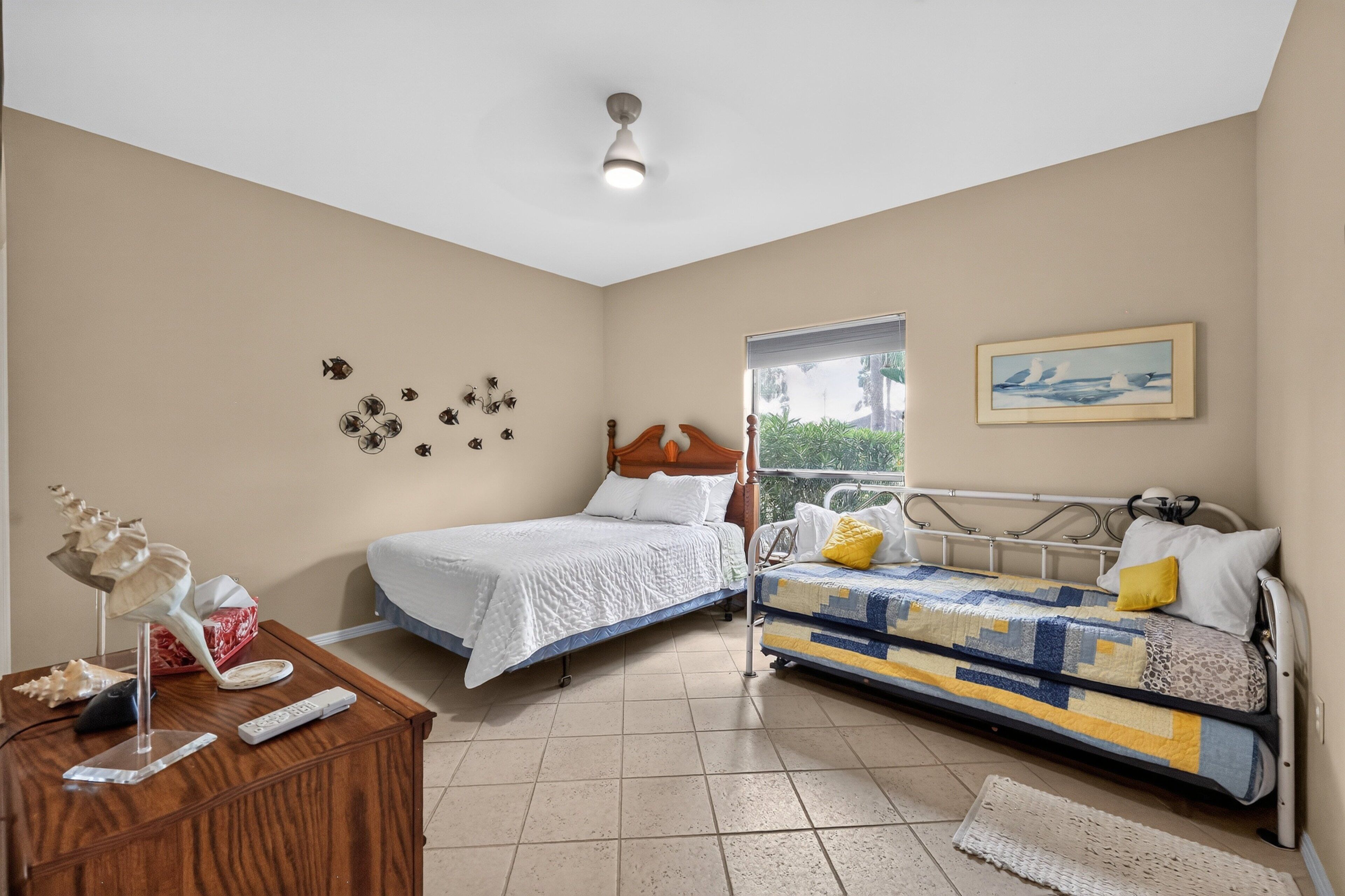 A bedroom with two beds, a wooden dresser, a ceiling light, a window, and wall decorations.