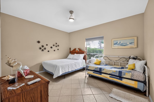 A bedroom with two beds, a wooden dresser, a ceiling light, a window, and wall decorations. - Laguna Vista Lakefront Retreat 2br Sleeps 6 2 Bedroom Townhouse (Port Isabel)