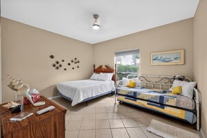 A bedroom with two beds, a wooden dresser, a ceiling light, a window, and wall decorations.