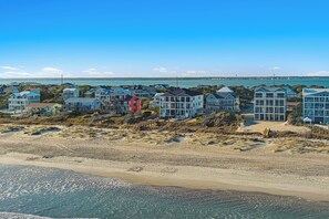 Een kustwoongebied met huizen direct aan het strand, waaronder woningen met balkons en een strand op de voorgrond.