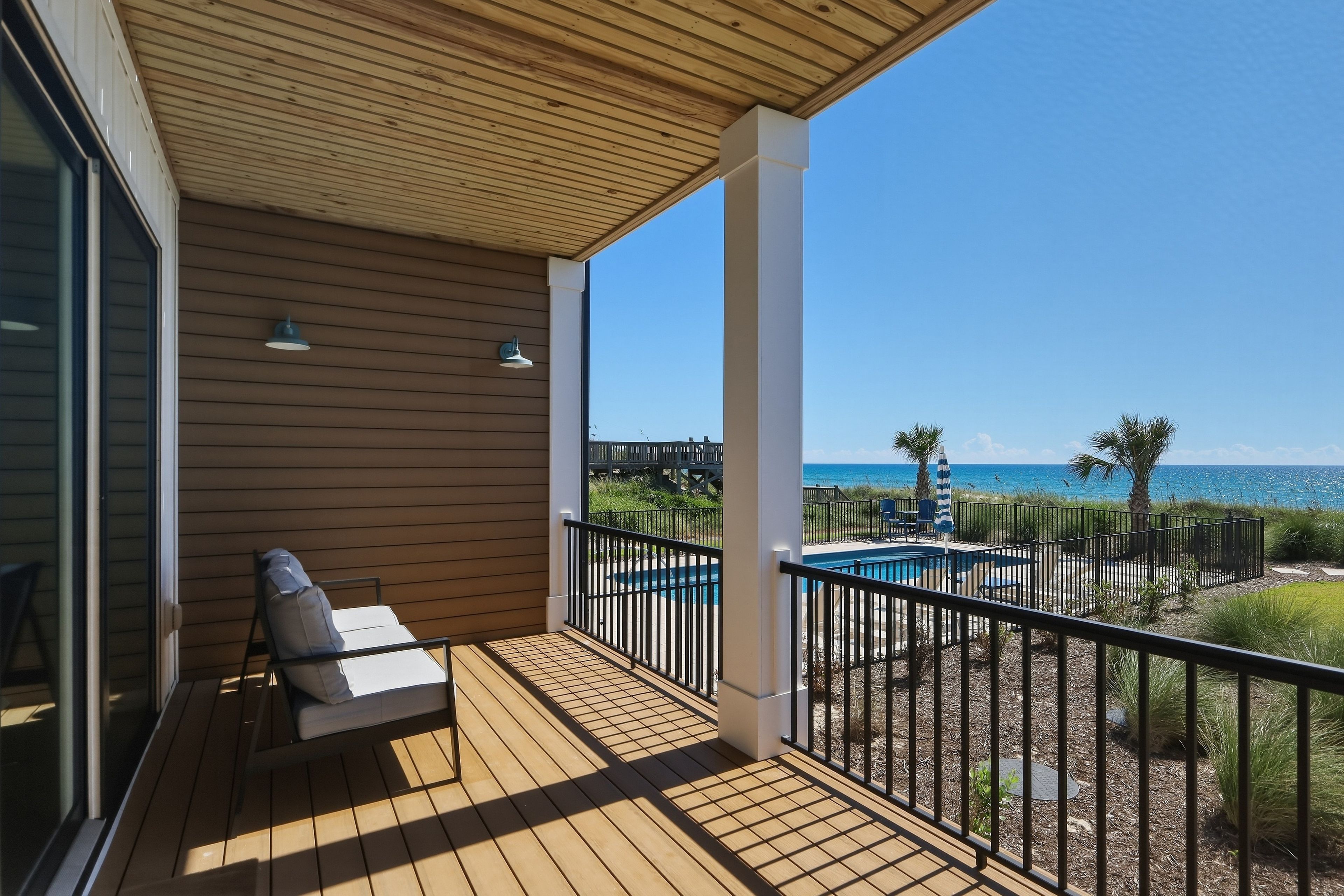 A wooden deck with a pool, lounge chairs, and a view of the ocean.