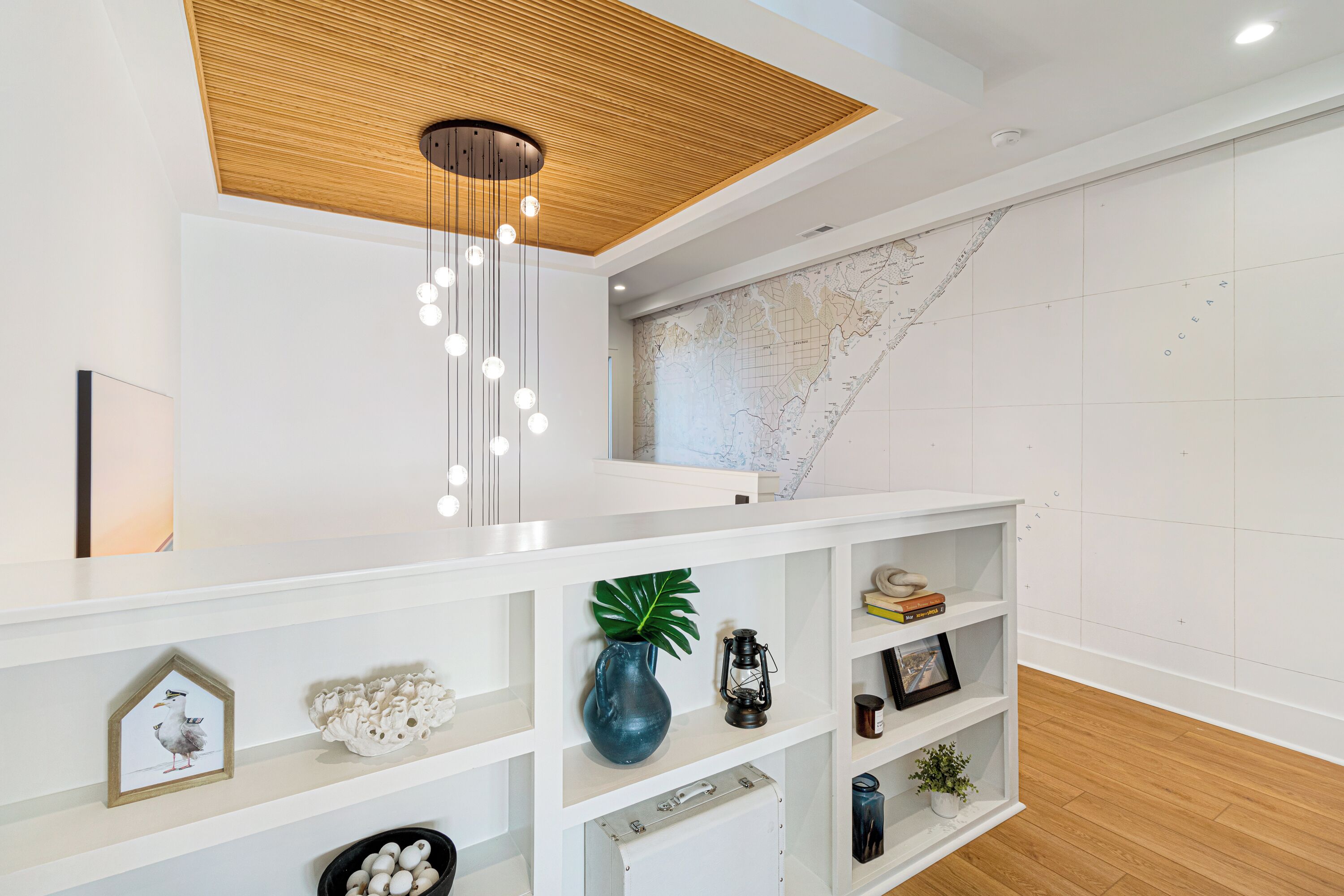 Ein modernes Interieur mit Holzbalkendecke, einer Karte an der Wand und einer weißen Regaleinheit mit verschiedenen Dekorationsobjekten.