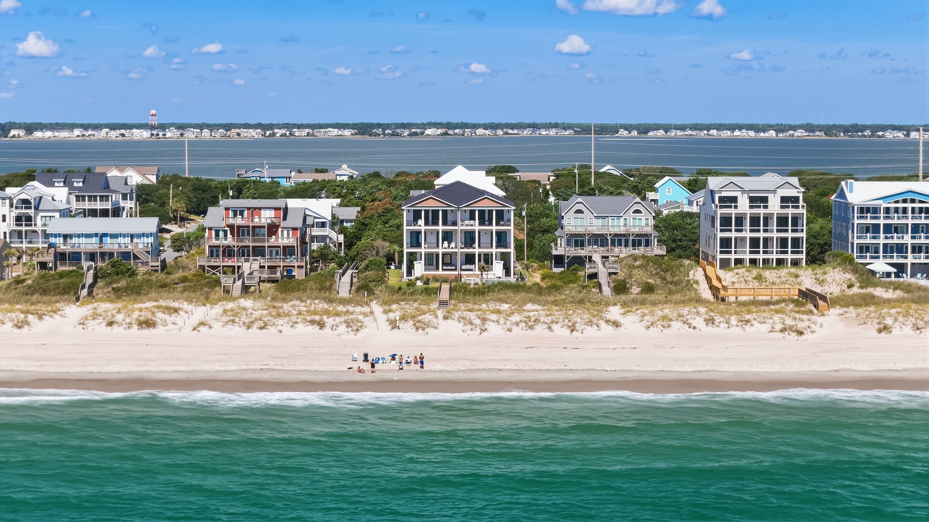 A beachfront property with multiple-story houses, a sandy beach, and a view of the ocean.