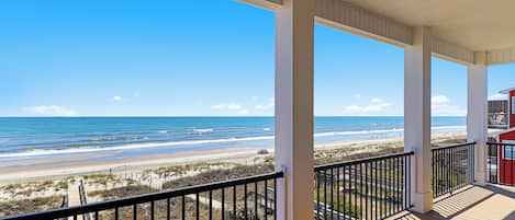 A covered balcony with a view of the beach and ocean.