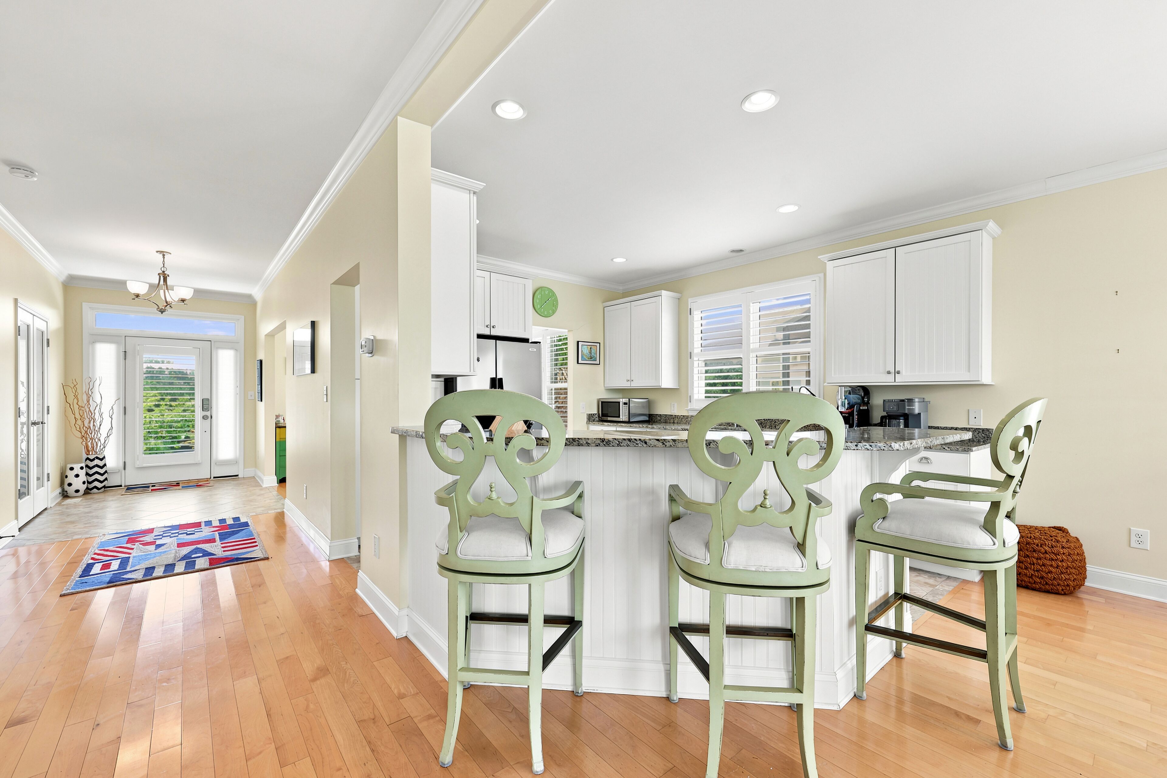 A modern kitchen with white cabinetry, a central island with bar stools, and a view to the outside.