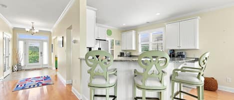 A modern kitchen with white cabinetry, a central island with bar stools, and a view to the outside.