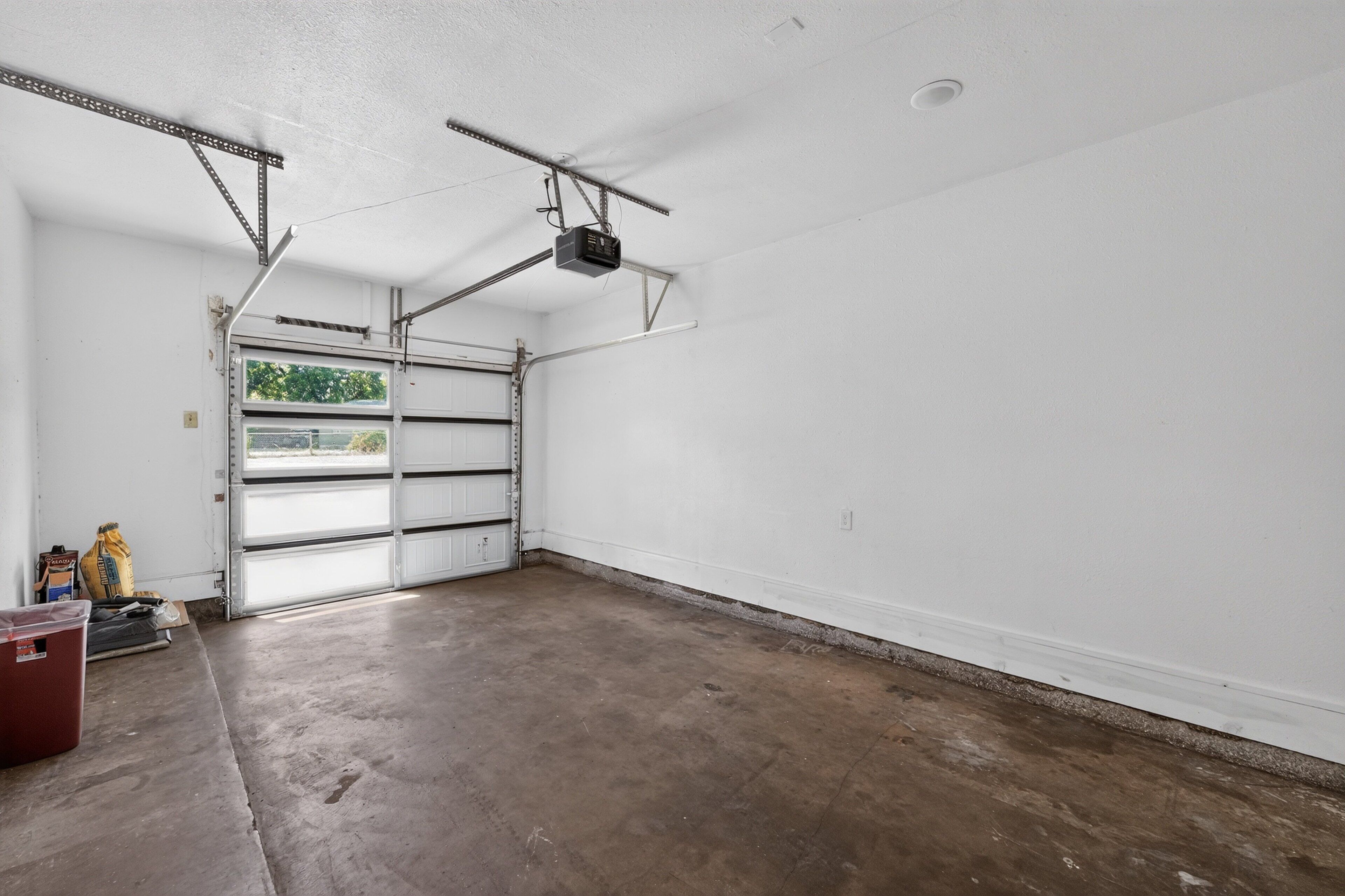 A garage with a white door, a ceiling-mounted projector, and a concrete floor.