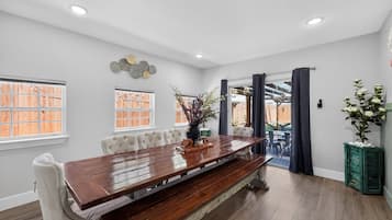 A dining area with a wooden table, white upholstered chairs, and a view to the outside.