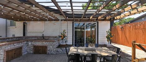 An outdoor patio with a stone fireplace, a dining table, and chairs.