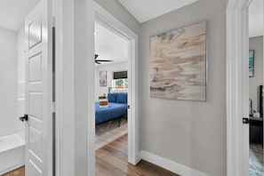 A hallway with a door leading to a room with a blue bed and a large abstract painting on the wall. - Firepit Family Basecamp Euless 3 Bedroom Home (Euless)