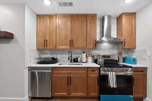 A modern kitchen with wooden cabinets, stainless steel appliances, and a tiled backsplash. - Firepit Family Basecamp Euless 3 Bedroom Home (Euless)