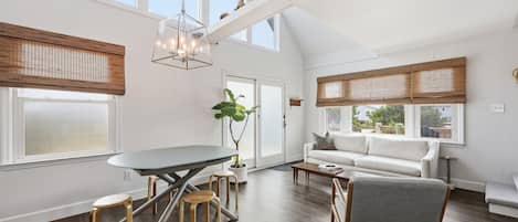 A spacious room with a dining table, chairs, a sofa, and a window with a view.