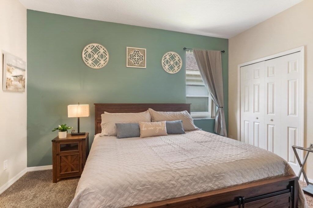 A bedroom with a bed, a nightstand with a lamp, decorative wall art, and a door.